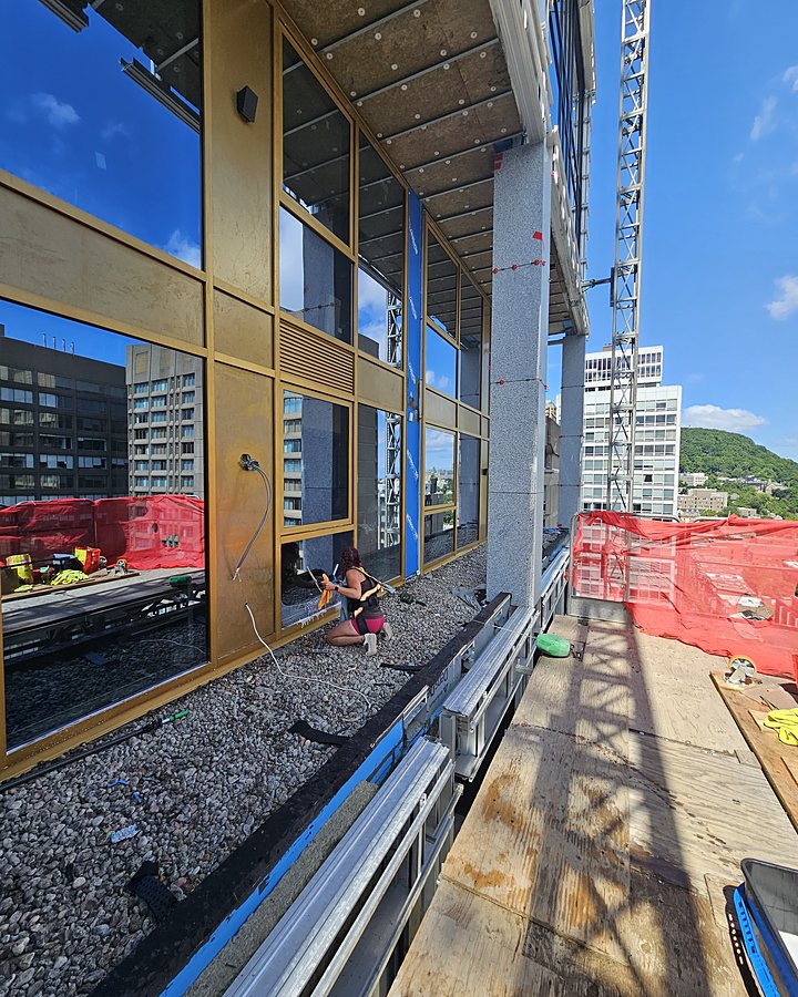 Technicien OMAX lavant un mur-rideau de verre sur un chantier de construction en hauteur