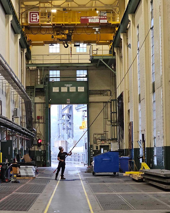 Technicien OMAX lavant les fenêtres d'une usine sous un pont roulant industriel