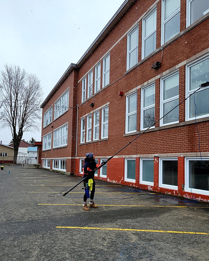 Technicien OMAX lavant les fenêtres d'une école en brique à la perche télescopique