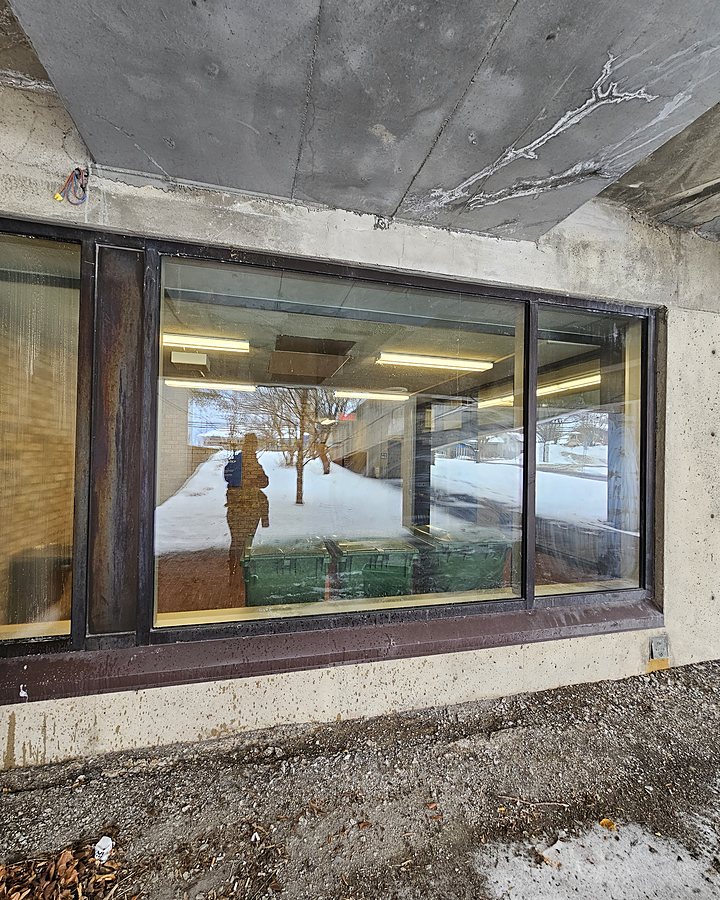 Vitrine d'un édifice institutionnel lavée en plein hiver, le technicien OMAX reflété dans la vitre