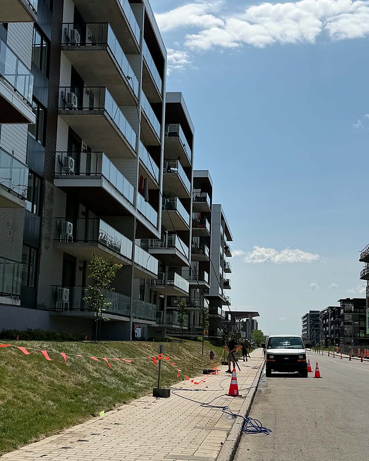 Chantier OMAX balisé de cônes devant une longue rangée de condos à balcons vitrés