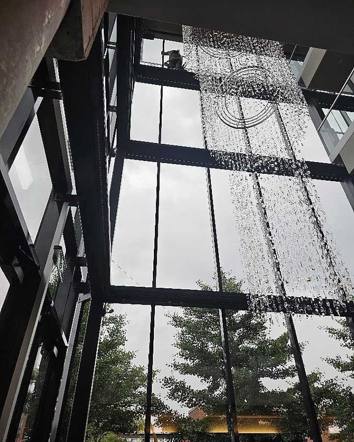 Technicien OMAX en hauteur à l'intérieur d'un atrium, lavant un mur-rideau vitré sur plusieurs étages