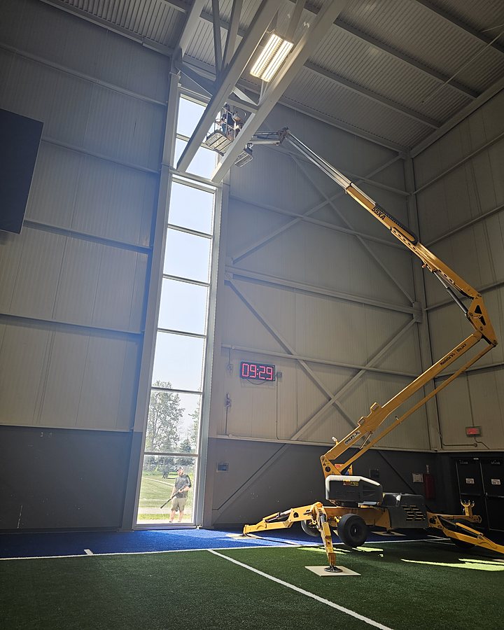 Nacelle articulée OMAX déployée à l'intérieur d'un complexe sportif pour laver une verrière de plusieurs étages